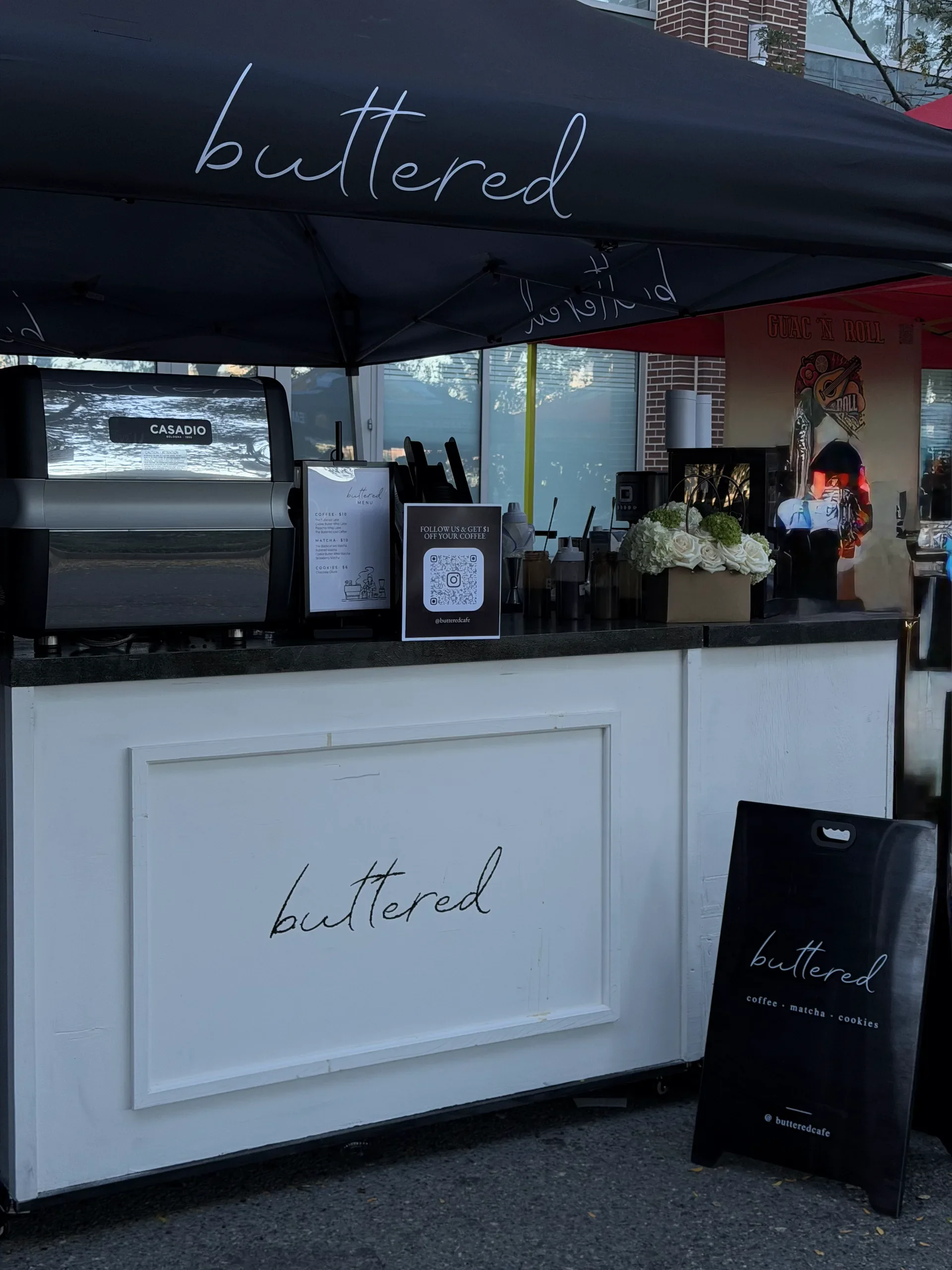 Buttered's stall under a black canopy, with an espresso machine, menu and sandwich board